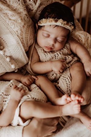 Close-up of sleeping baby wearing vintage lace clothing against soft textiles.