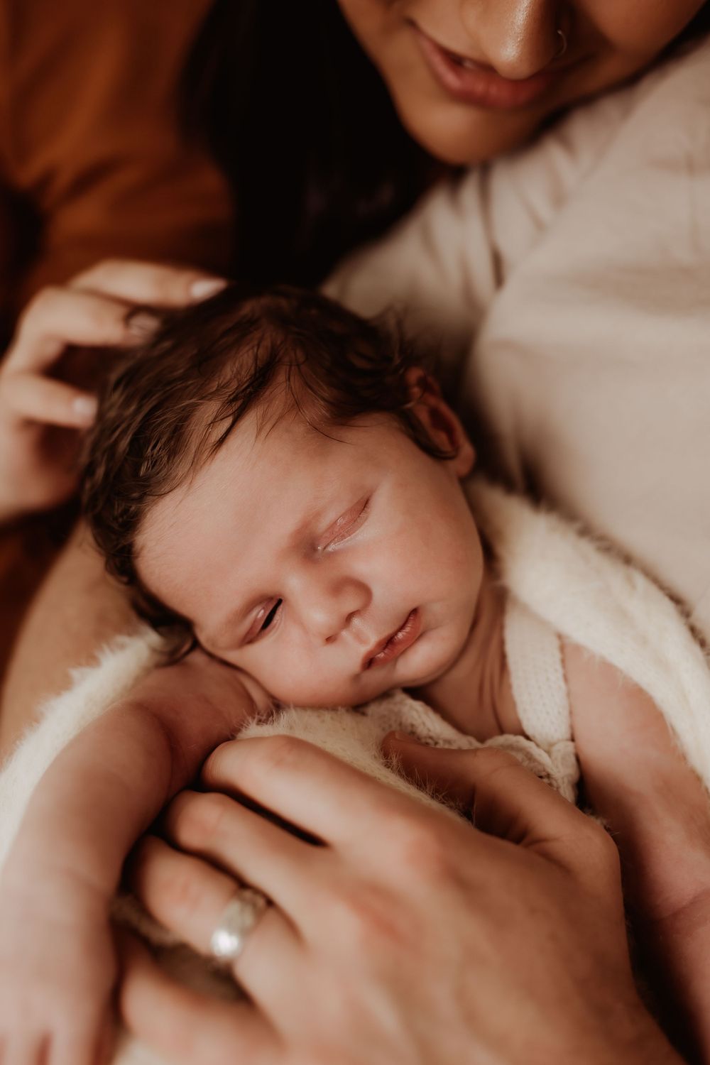 Tender moment of parents holding their sleeping newborn wrapped in white.