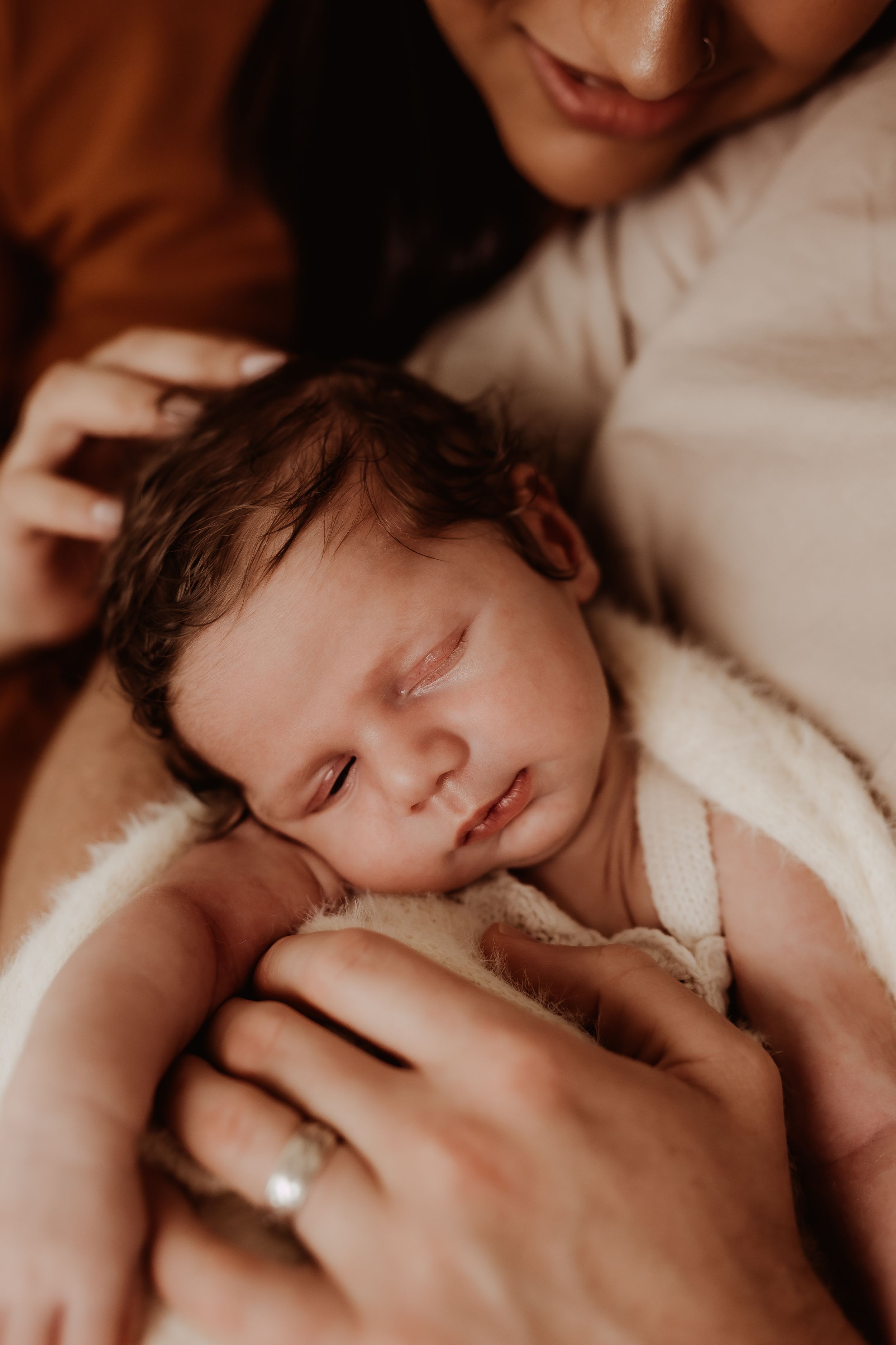 Tender moment of parents holding their sleeping newborn wrapped in white.