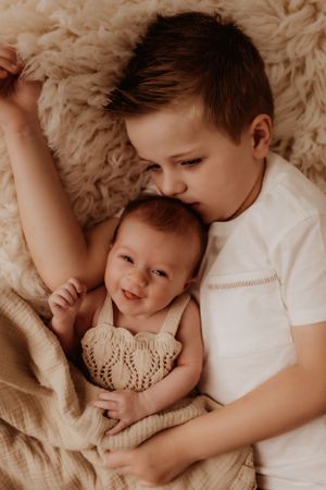 Two siblings sharing a tender moment while cuddling on soft furry blankets.