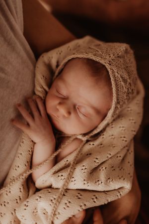 Sleeping newborn wrapped in delicate lace blanket captured in warm sepia tones.