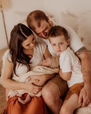 Family cuddle session on bed wearing coordinated white and earth-toned clothing.