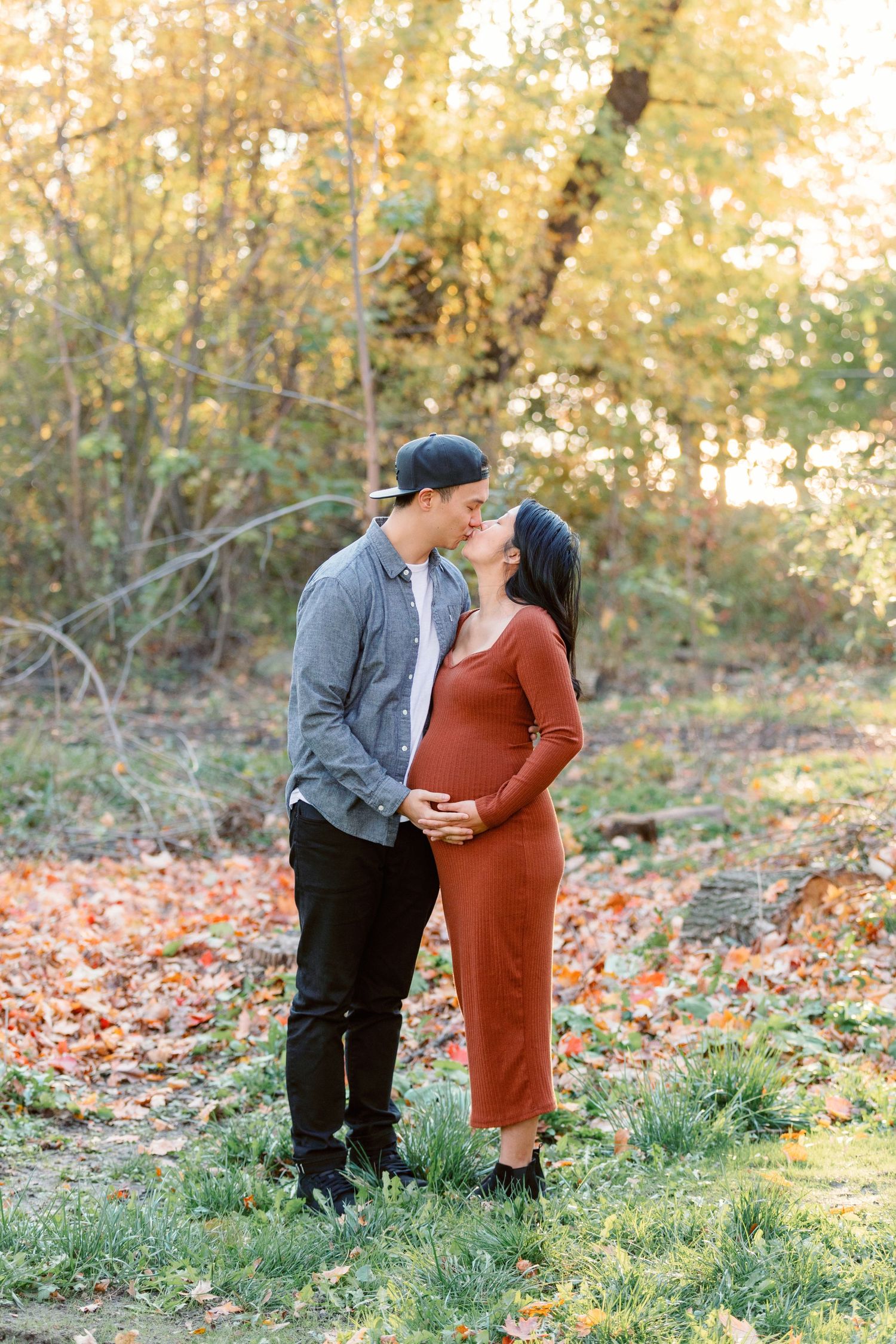 A pregnant couple kissing in a leafy field captured by Toronto wedding photographer Katie Crane at Guild Inn Estate.