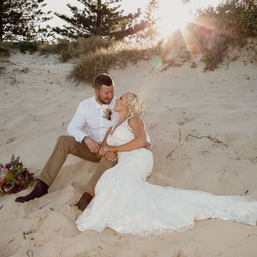 Lovely sunset with bride and groom sitting in the sand looking at each other.