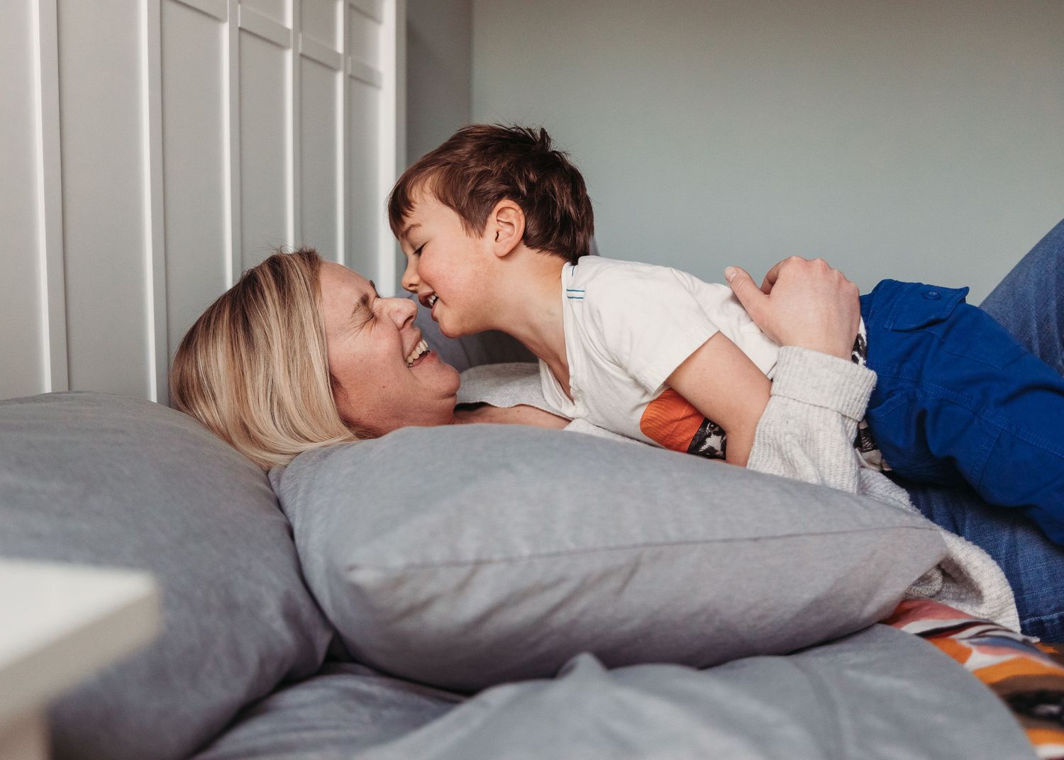 A tender moment of connection and laughter shared on a bed with a gray pillow.