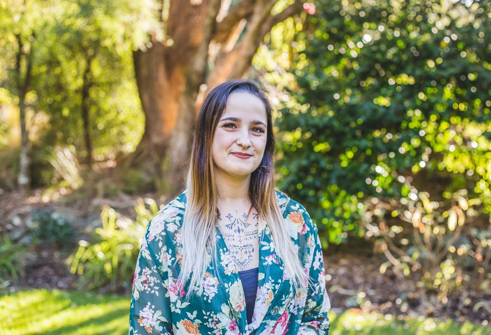 A person in a floral green top poses outdoors with a genuine smile against a natural backdrop.