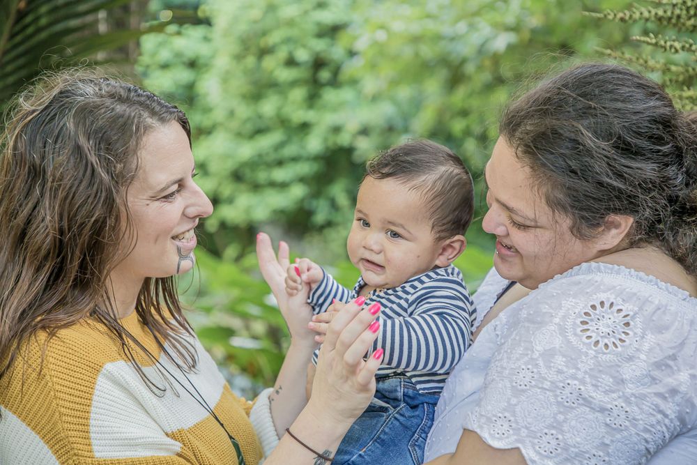 Joyful outdoor family interaction with yellow sweater detail against green foliage.