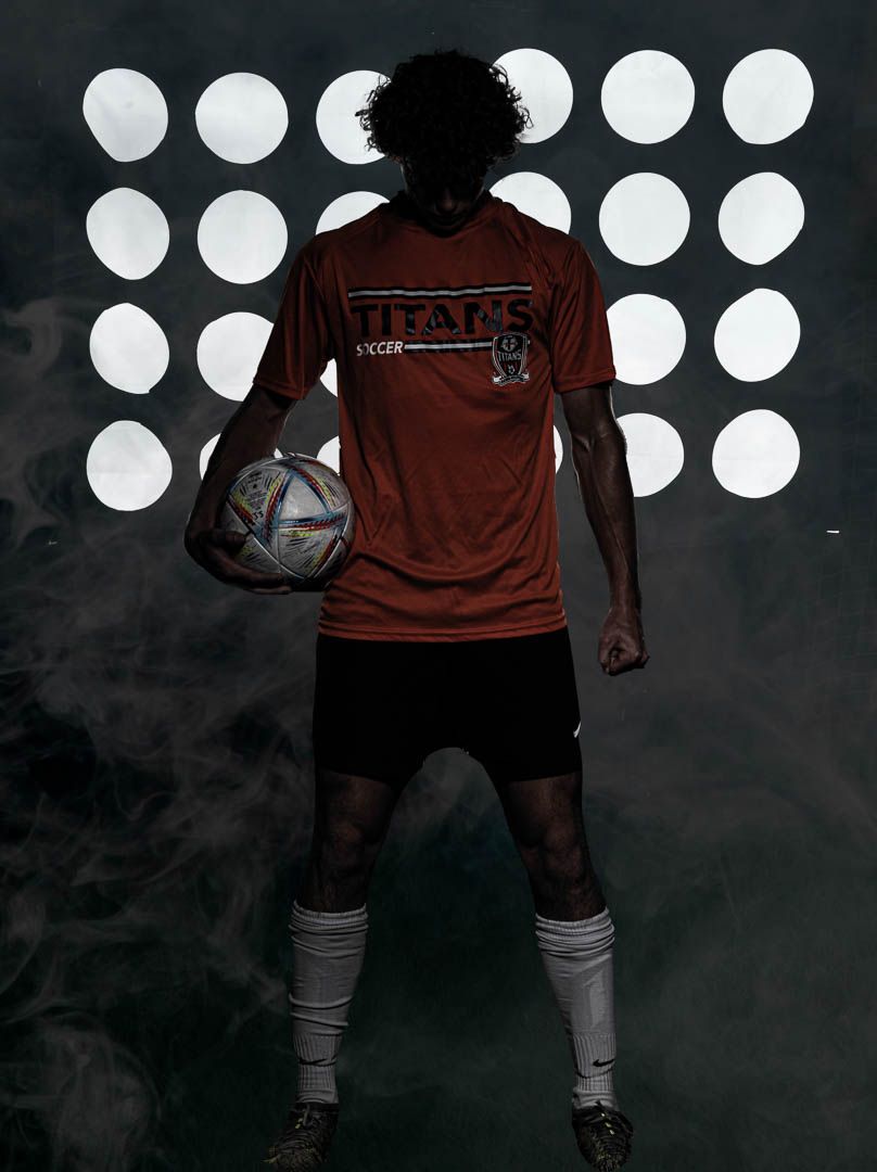 Athletic silhouette in red jersey poses dramatically against glowing white circles and smoky background with soccer ball.