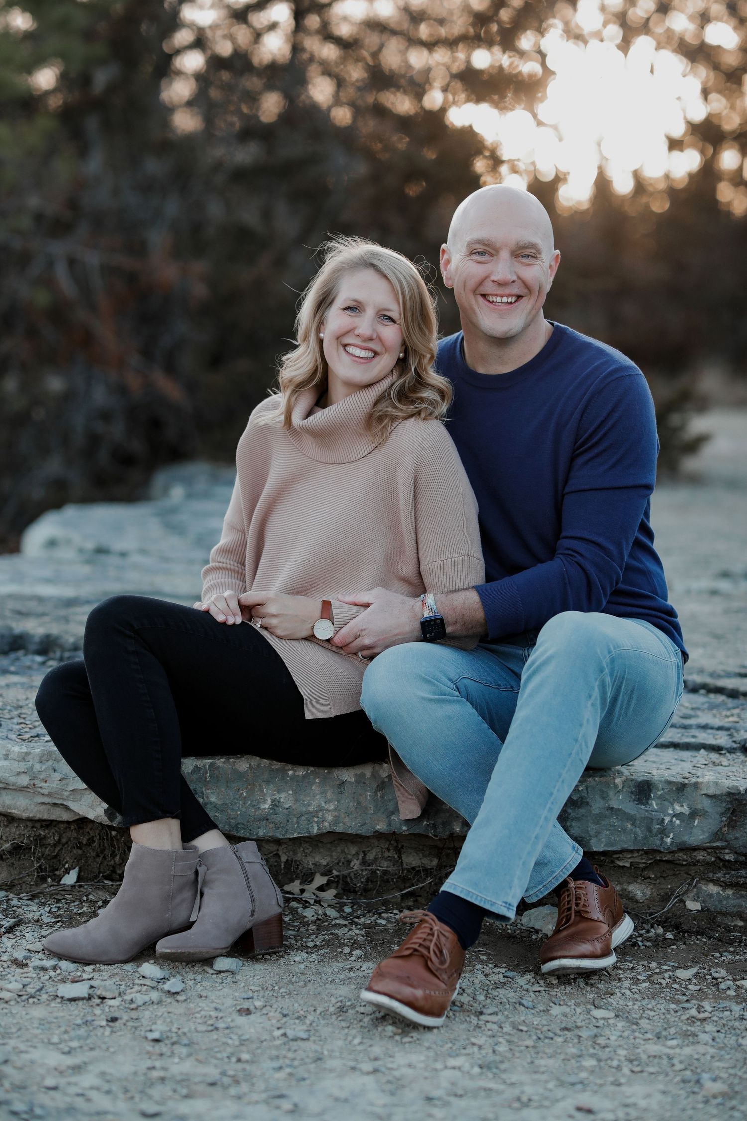 Smiling couple sitting on rocks at sunset in casual outdoor portrait.