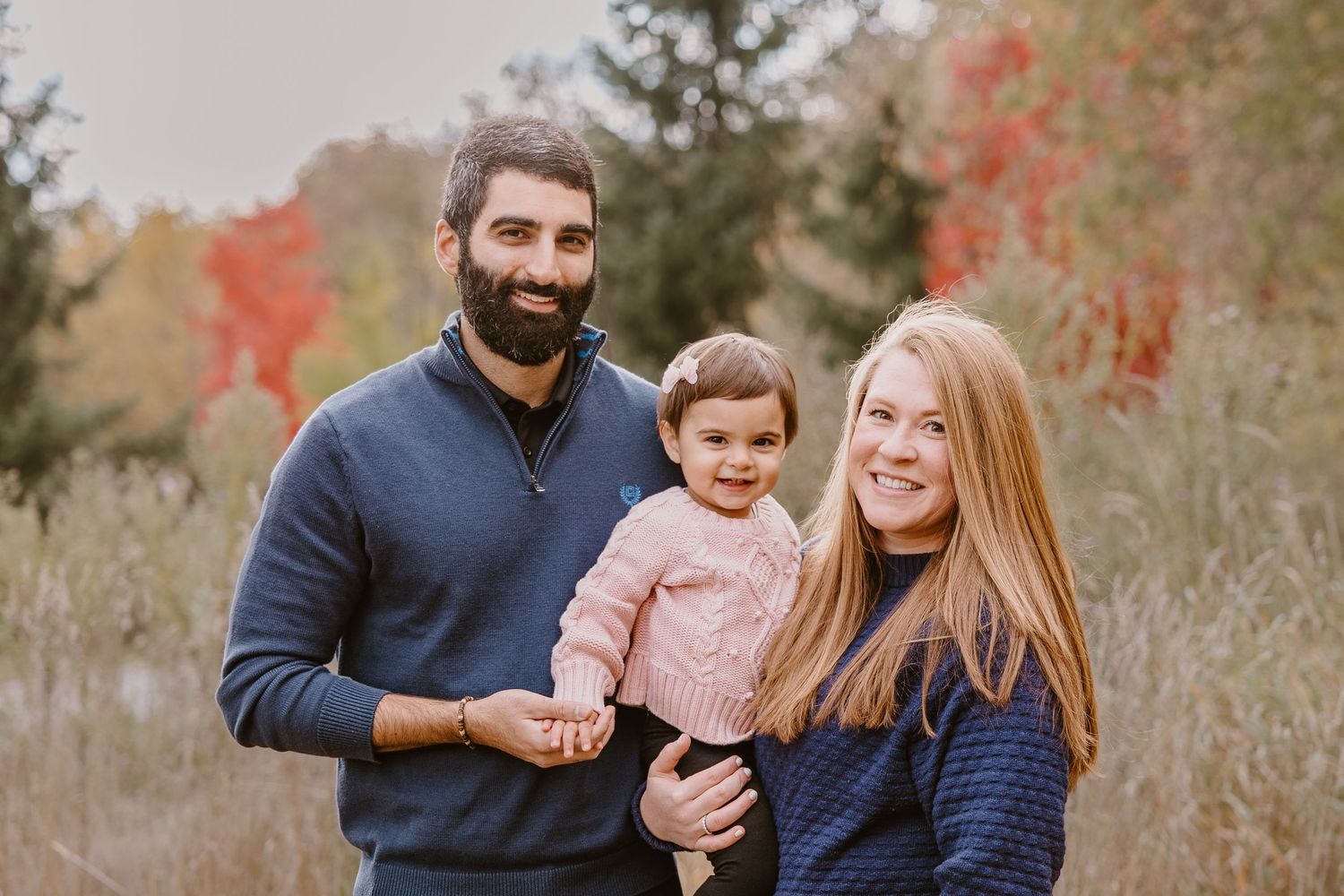 A family poses together on a path with beautiful fall foliage in the background.