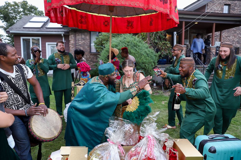 Musicians in green robes perform with drums under a red canopy at an outdoor celebration.