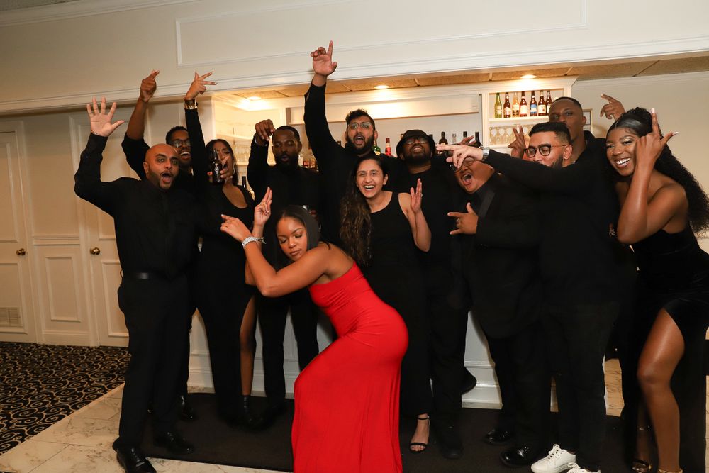 A group in formal black attire celebrates enthusiastically at an indoor party.