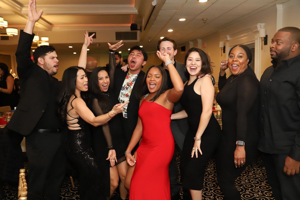 Party guests dance and celebrate in formal attire at an indoor event.