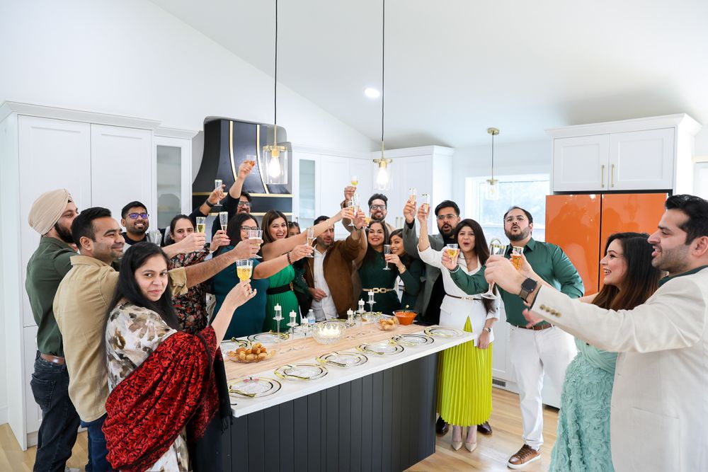 A group celebrates together in a modern kitchen with raised glasses during a toast.
