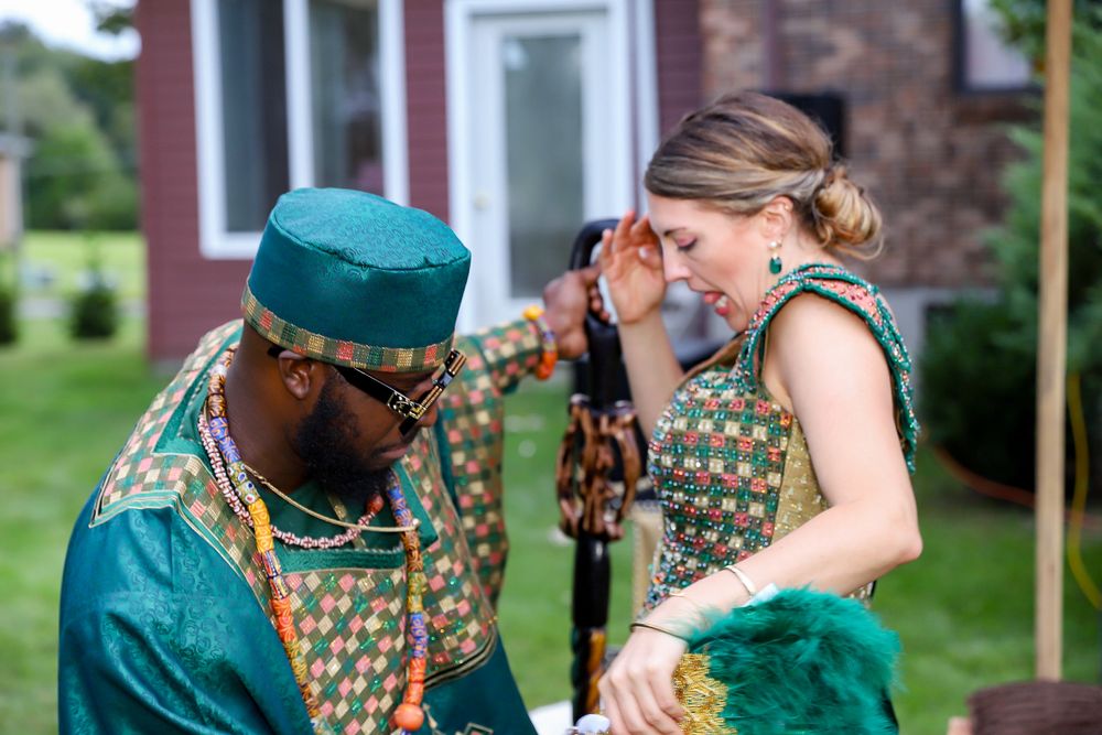 A couple in matching green and gold patterned outfits dance at an outdoor celebration.