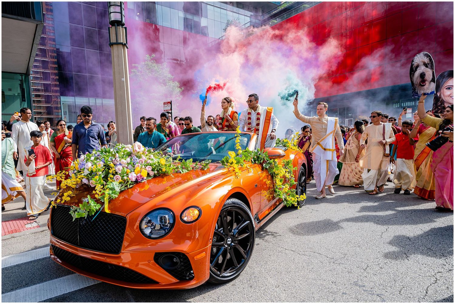 Festive street celebration with orange sports car and colorful smoke effects.