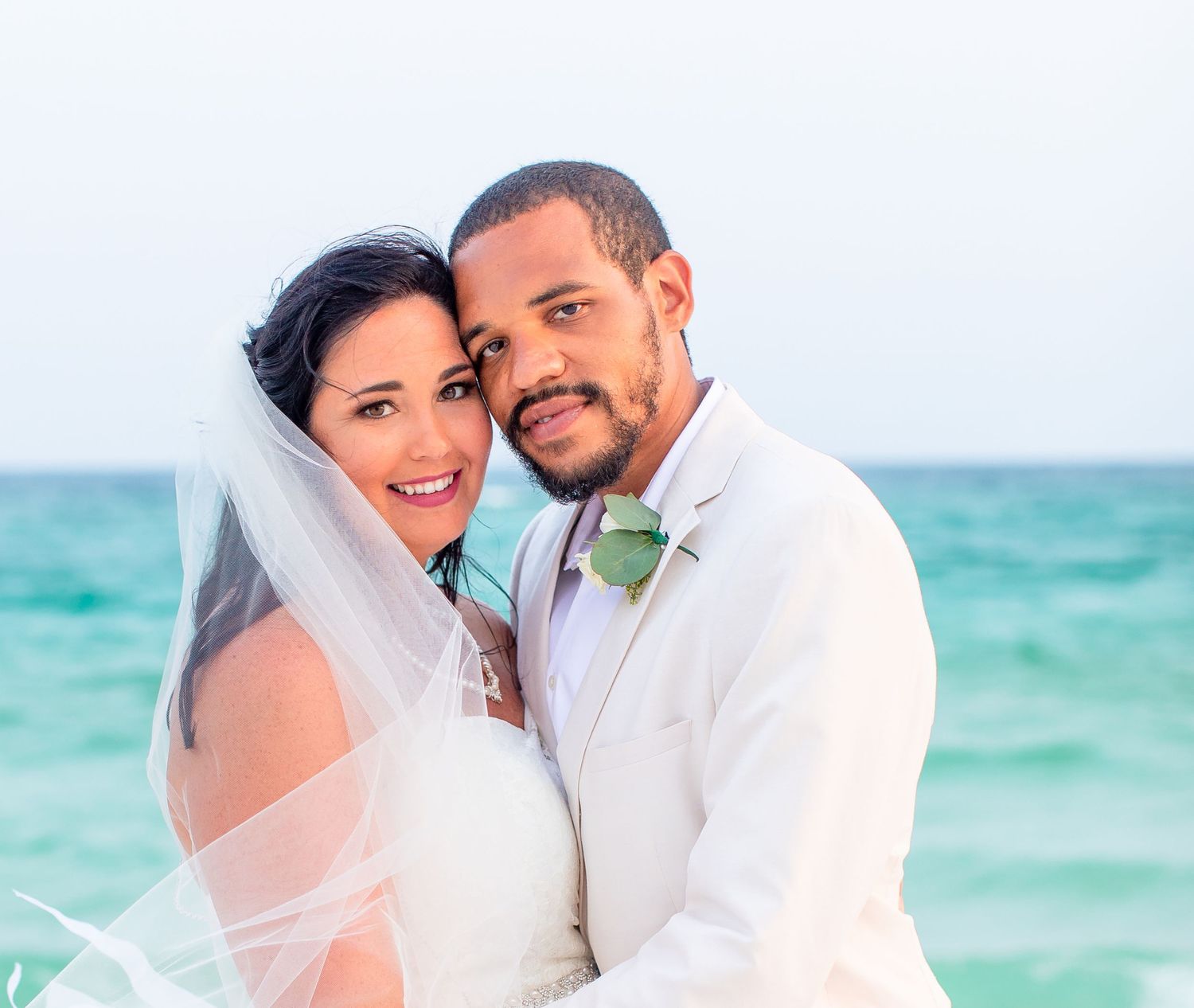 Beach wedding portrait with turquoise ocean backdrop and elegant white attire.