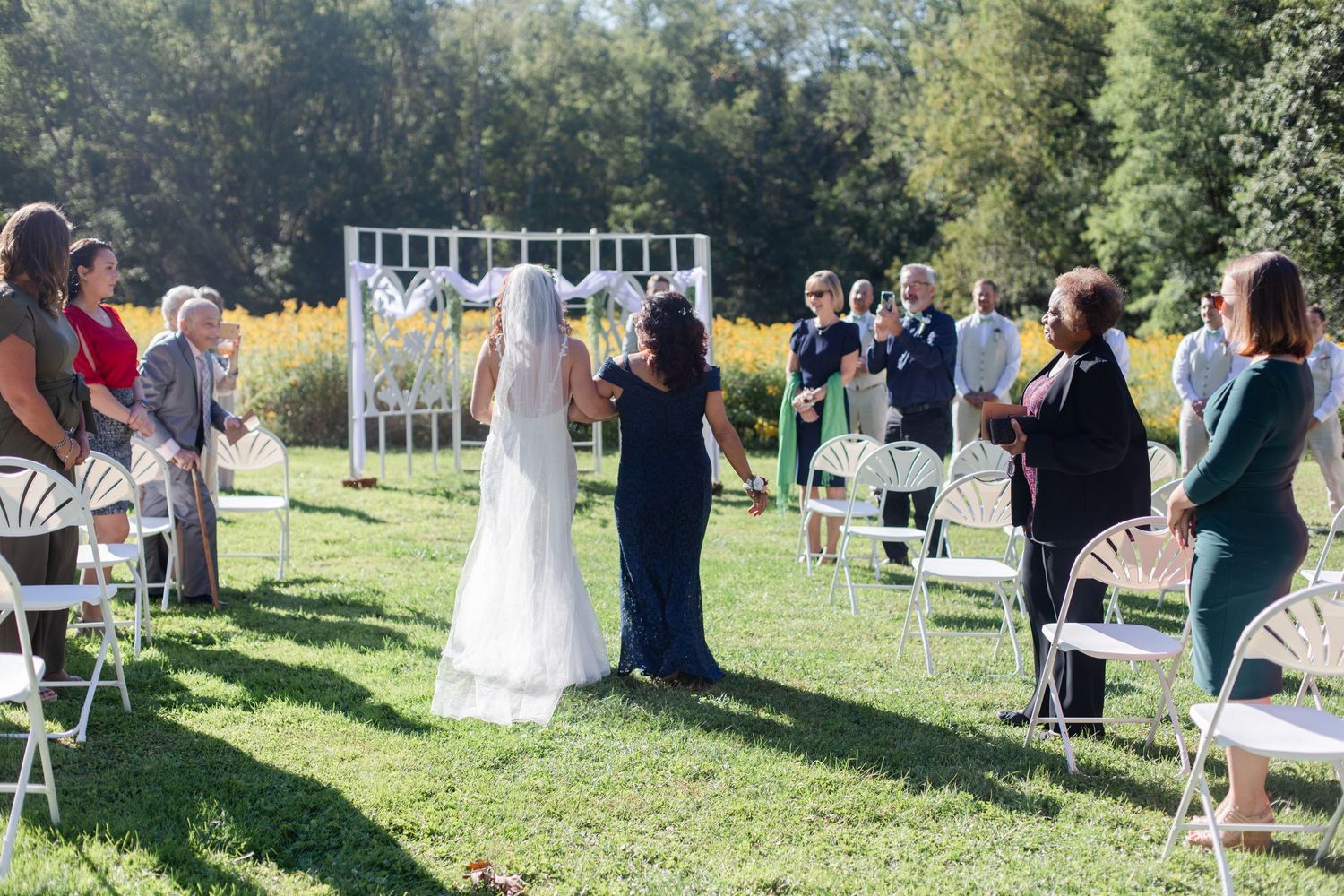 An outdoor wedding ceremony setup with white chairs and decorations in a grassy field.