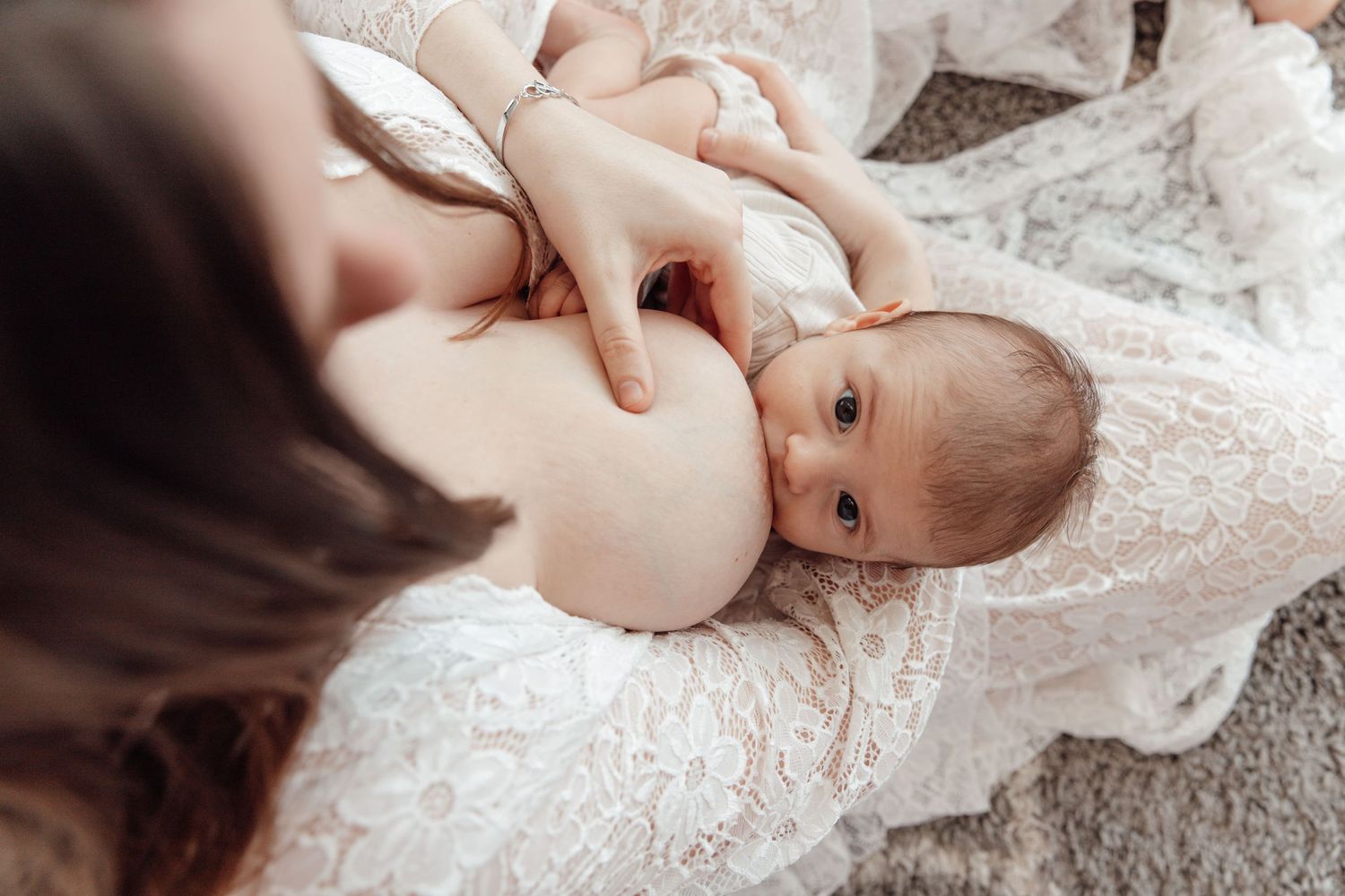 Baby lying on white lace fabric looking up at camera.