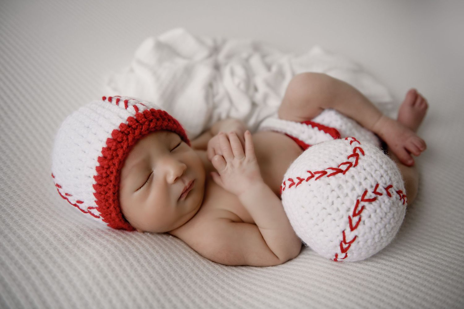 Newborn baby sleeping peacefully in baseball-themed knit outfit.