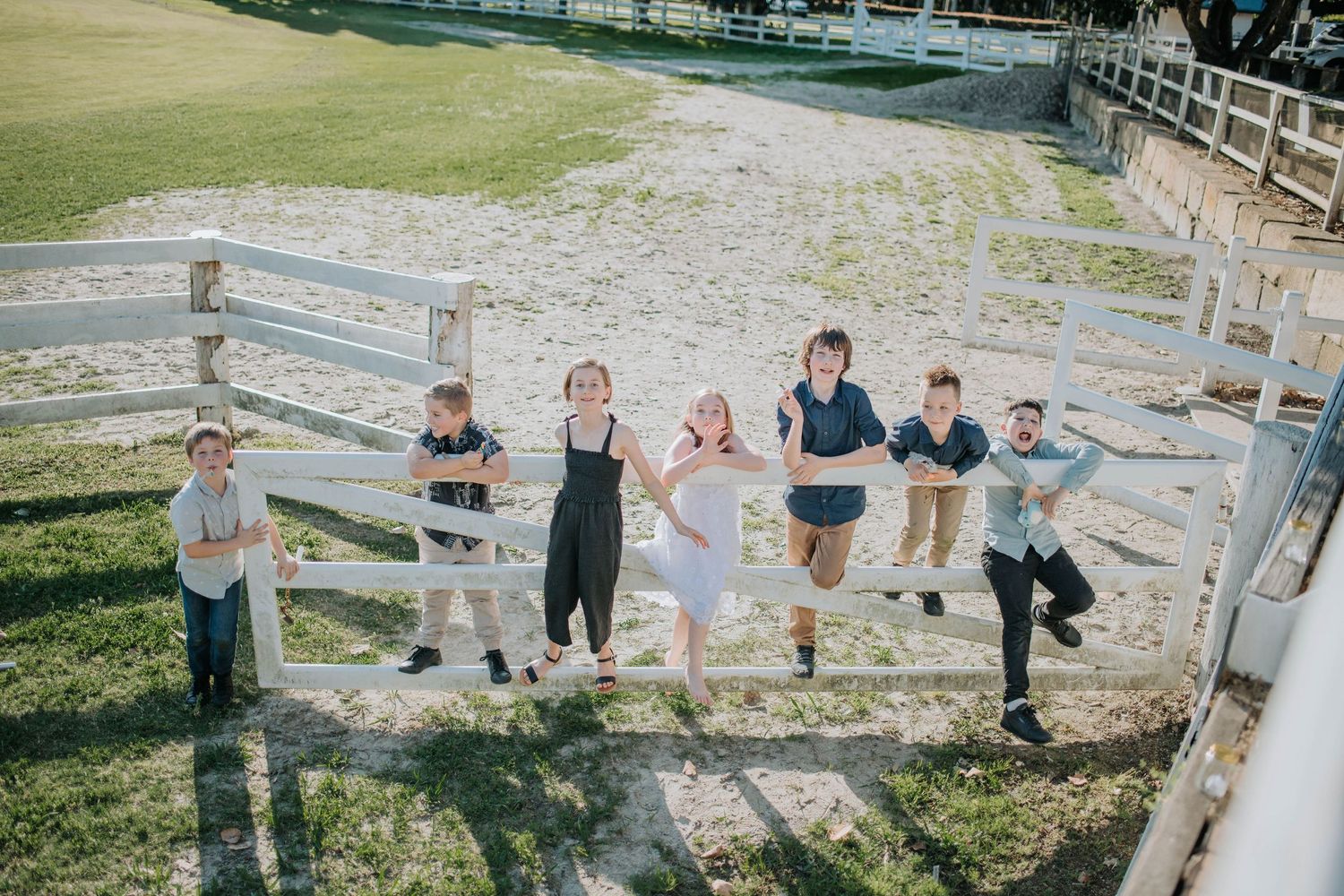 A group of people balancing on a white wooden fence at an outdoor venue.