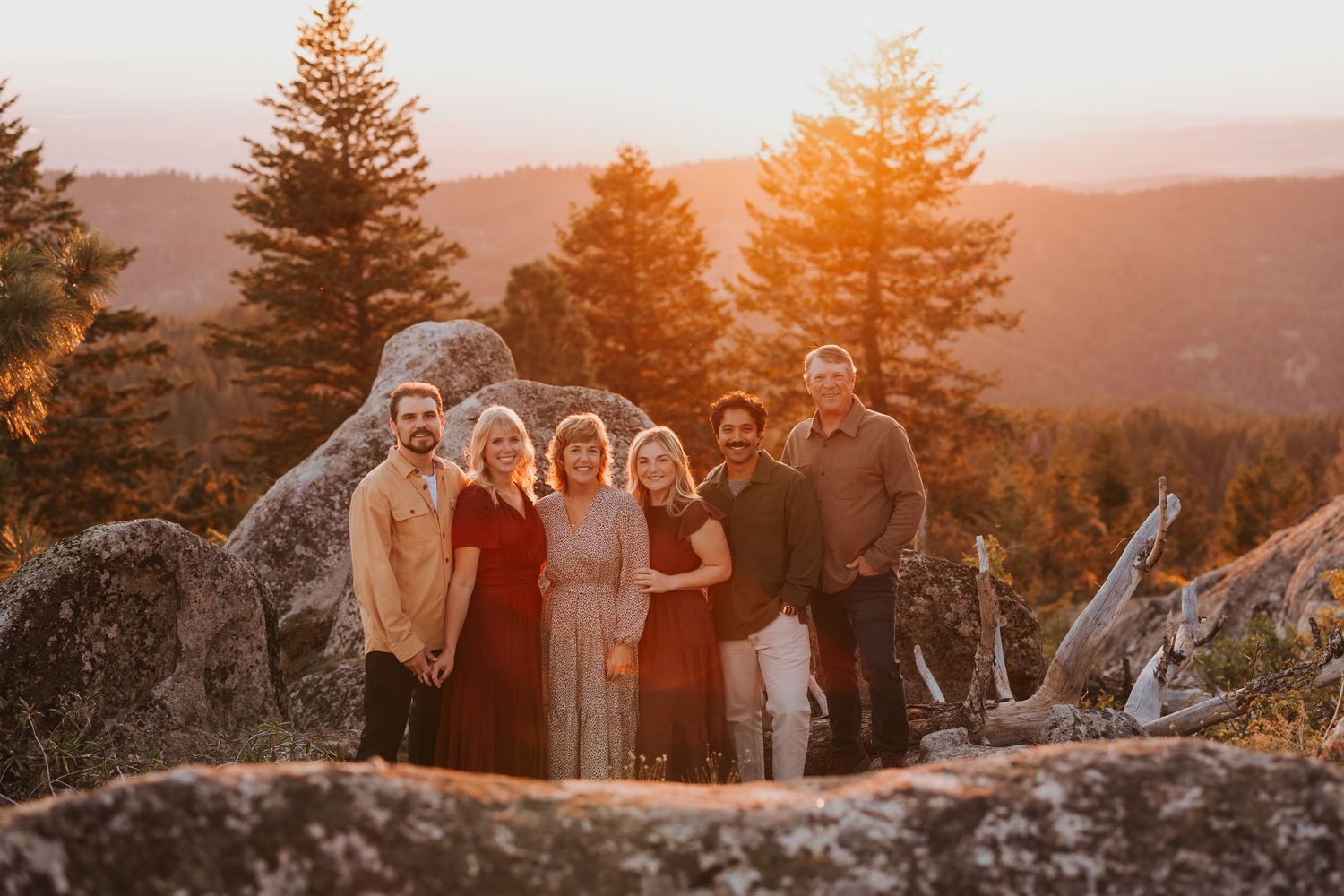 A group poses on rocky terrain during sunset with pine trees in the background.