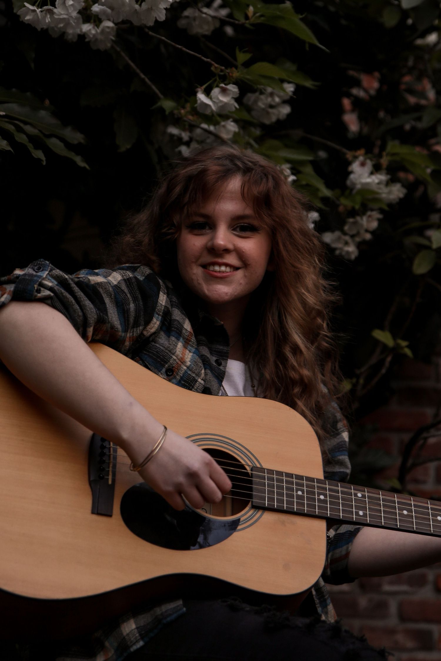 Person playing acoustic guitar outdoors with cherry blossoms in background.