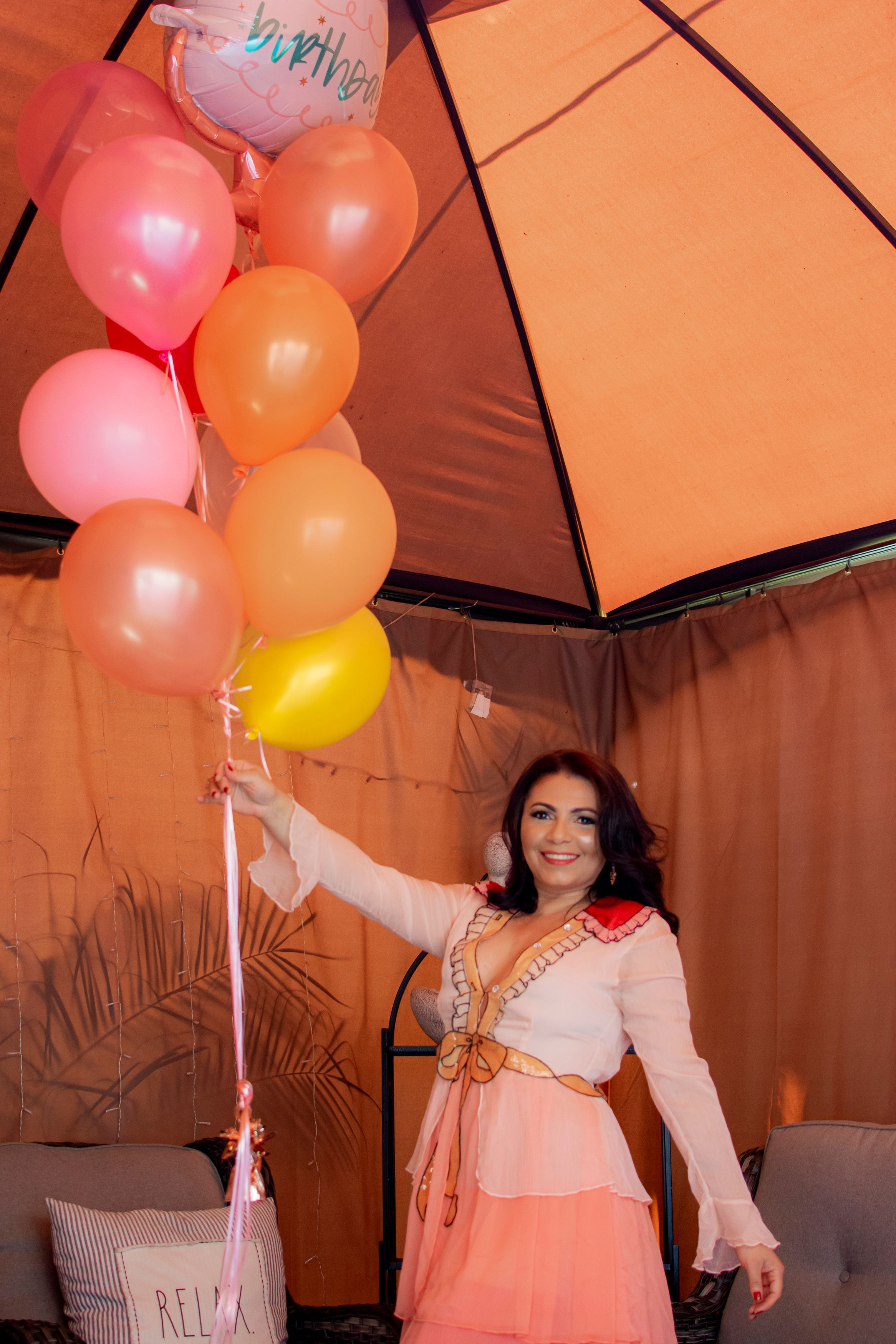 Celebratory scene with colorful balloons and pink ombre dress under an orange umbrella canopy.