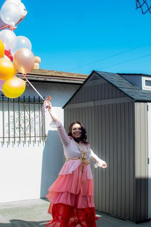 Festive outdoor celebration with pastel balloons against bright blue sky and gray building.