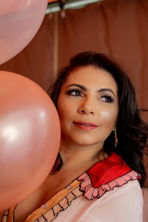 Close-up portrait with soft pink balloon and delicate ruffled dress details.