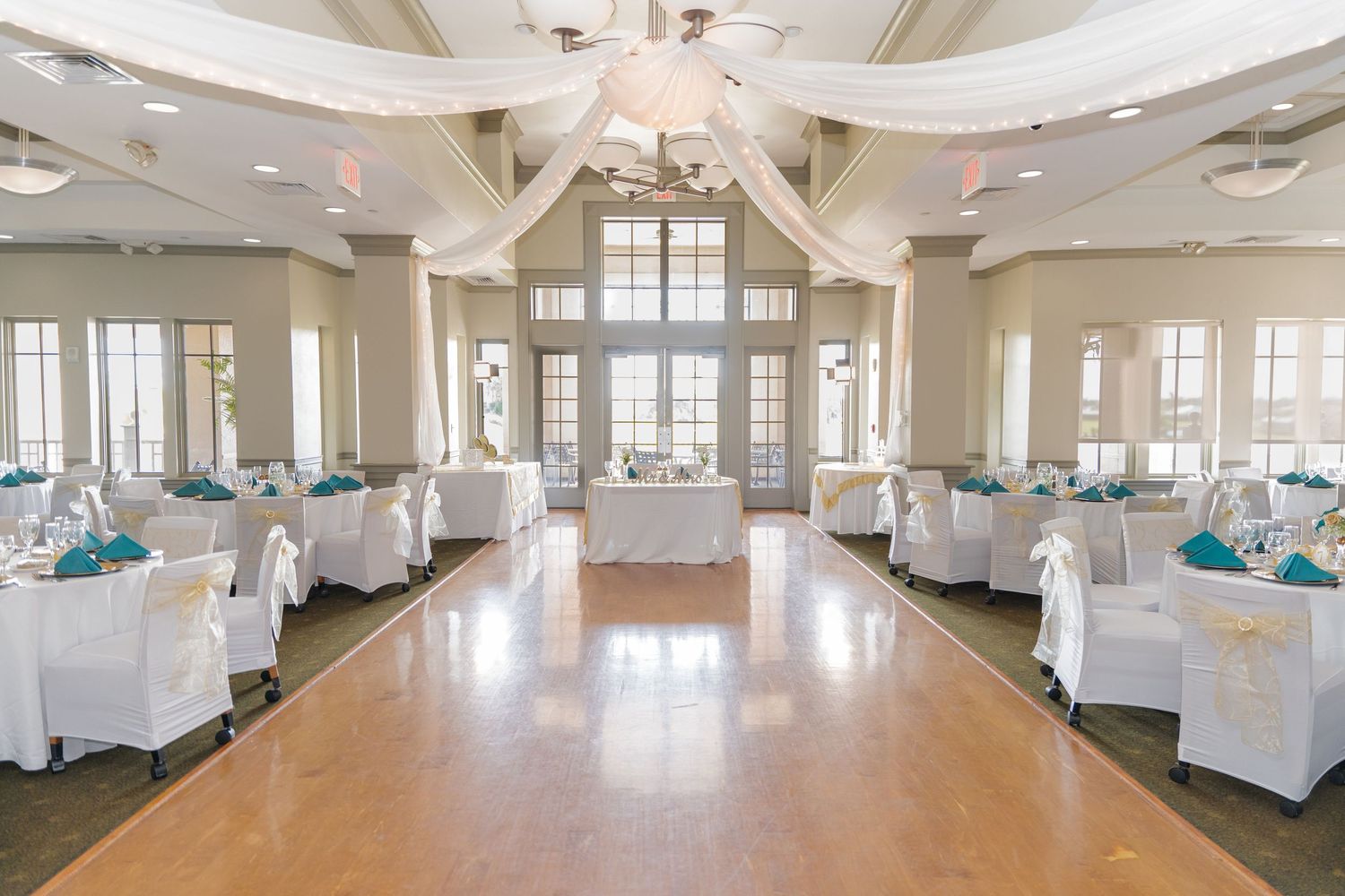 Elegant wedding venue interior with white chairs and teal accents under vaulted ceilings.