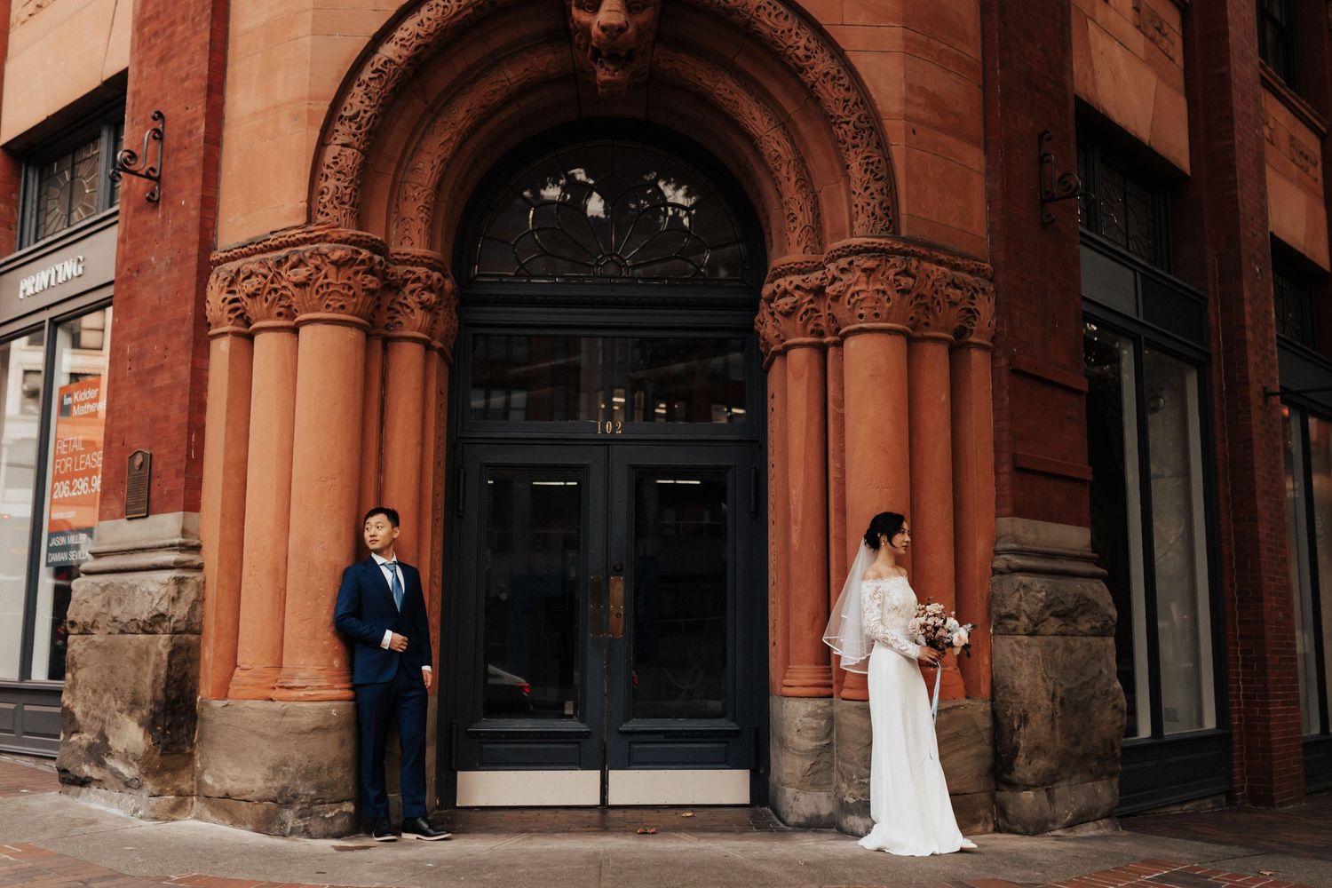 A couple poses separately against red brick architecture with ornate details.