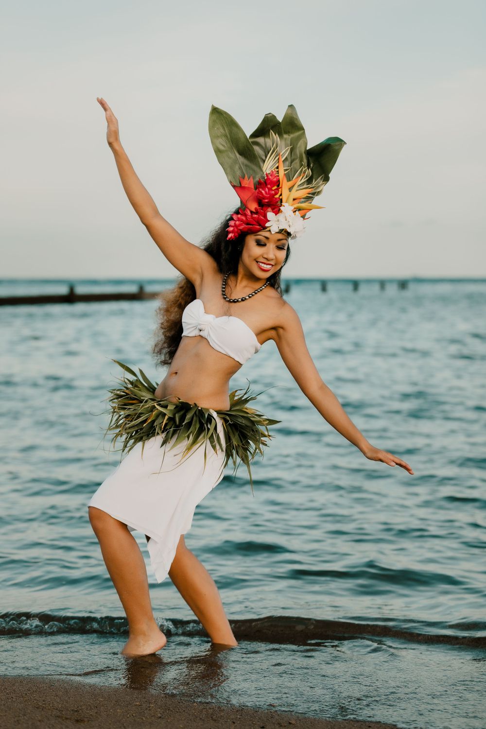 Hula dancer in traditional costume performs graceful dance moves at the beach during sunset.