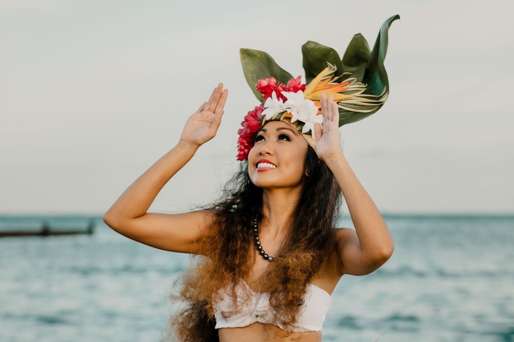 Dancer in tropical headdress poses against ocean backdrop.