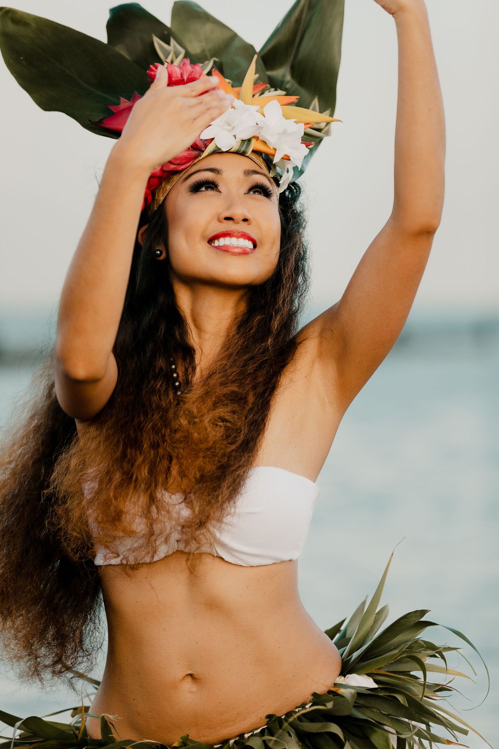 Dancer in traditional Hawaiian costume with floral headdress at sunset.