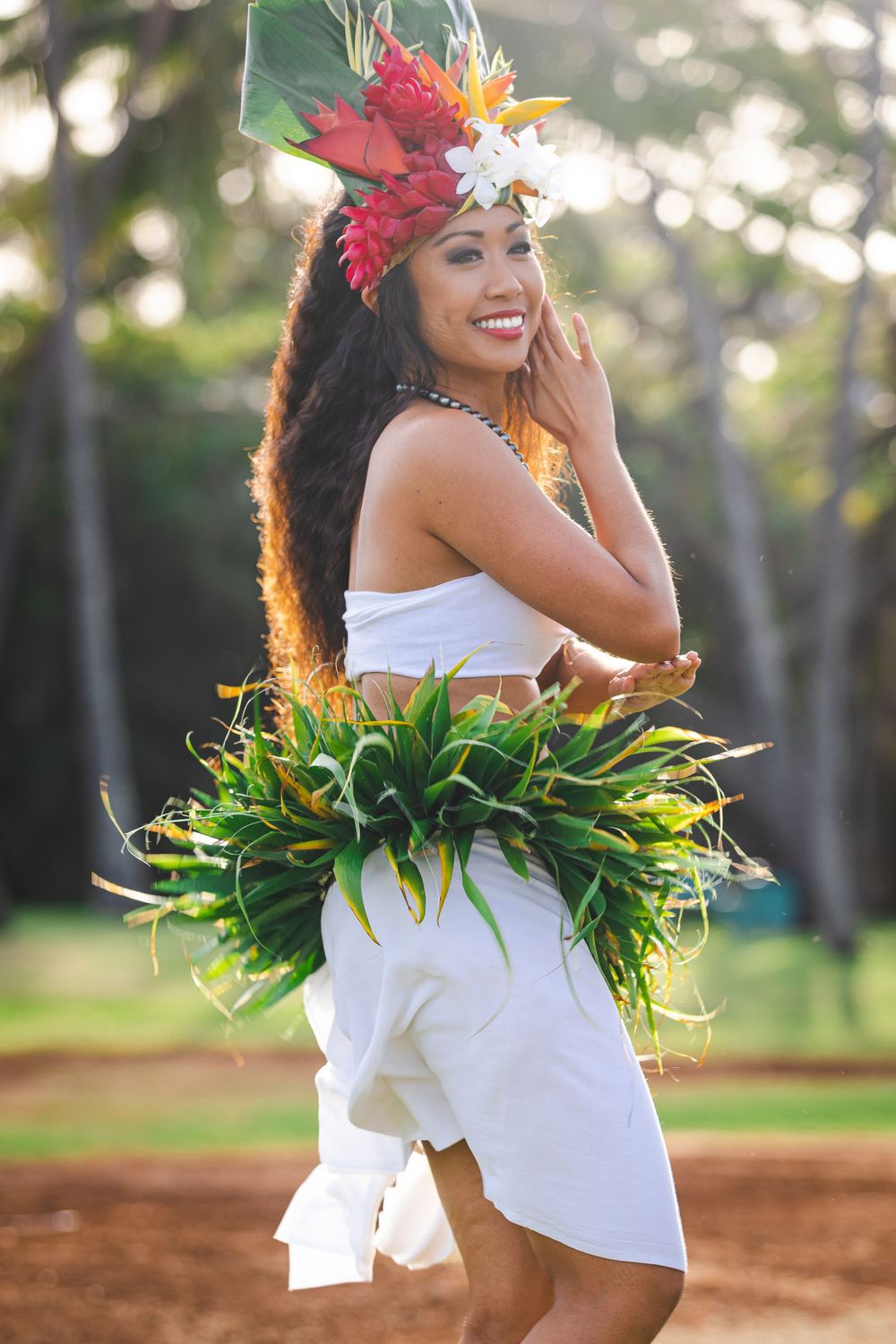 Dancer in white outfit and floral headdress performing traditional Hawaiian dance.