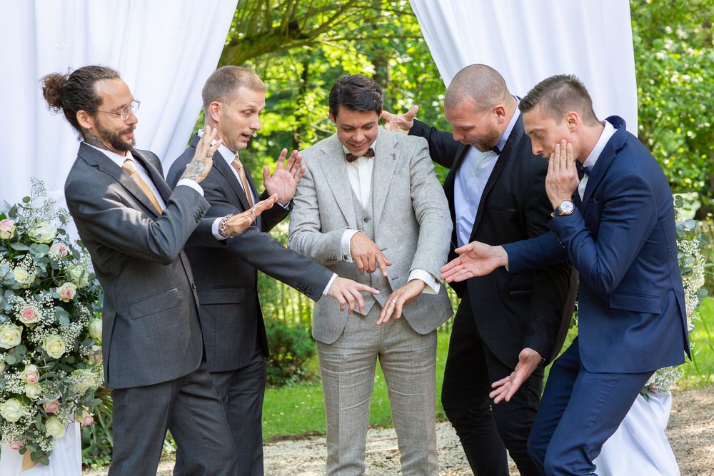 Groomsmen sharing a lighthearted moment during an outdoor wedding ceremony with floral decorations.