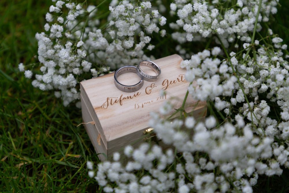Wedding rings displayed on wooden box surrounded by delicate white flowers.