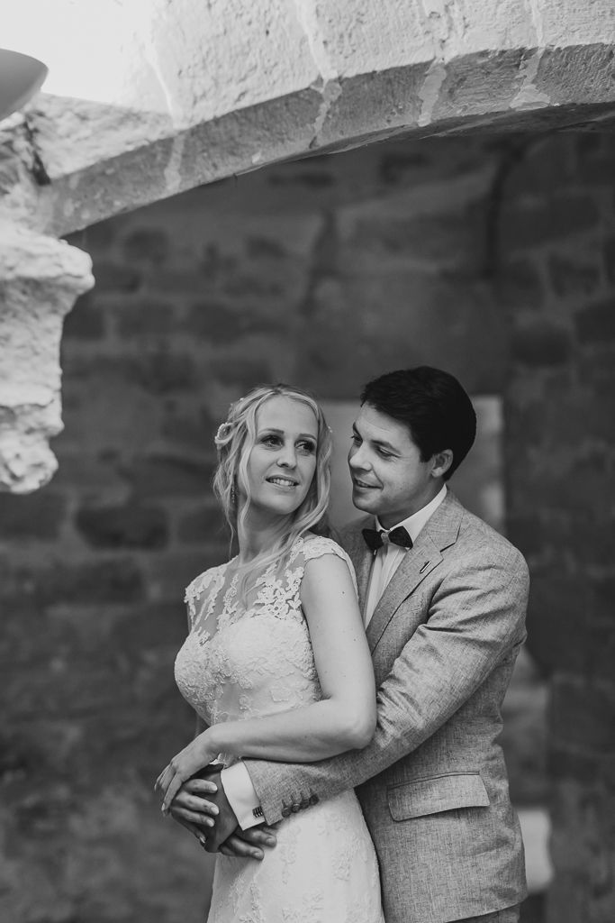 Black and white portrait of couple against rustic stone wall architecture.