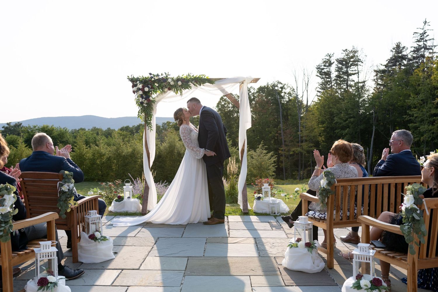 Outdoor wedding ceremony under floral arch with mountain views and seated guests.