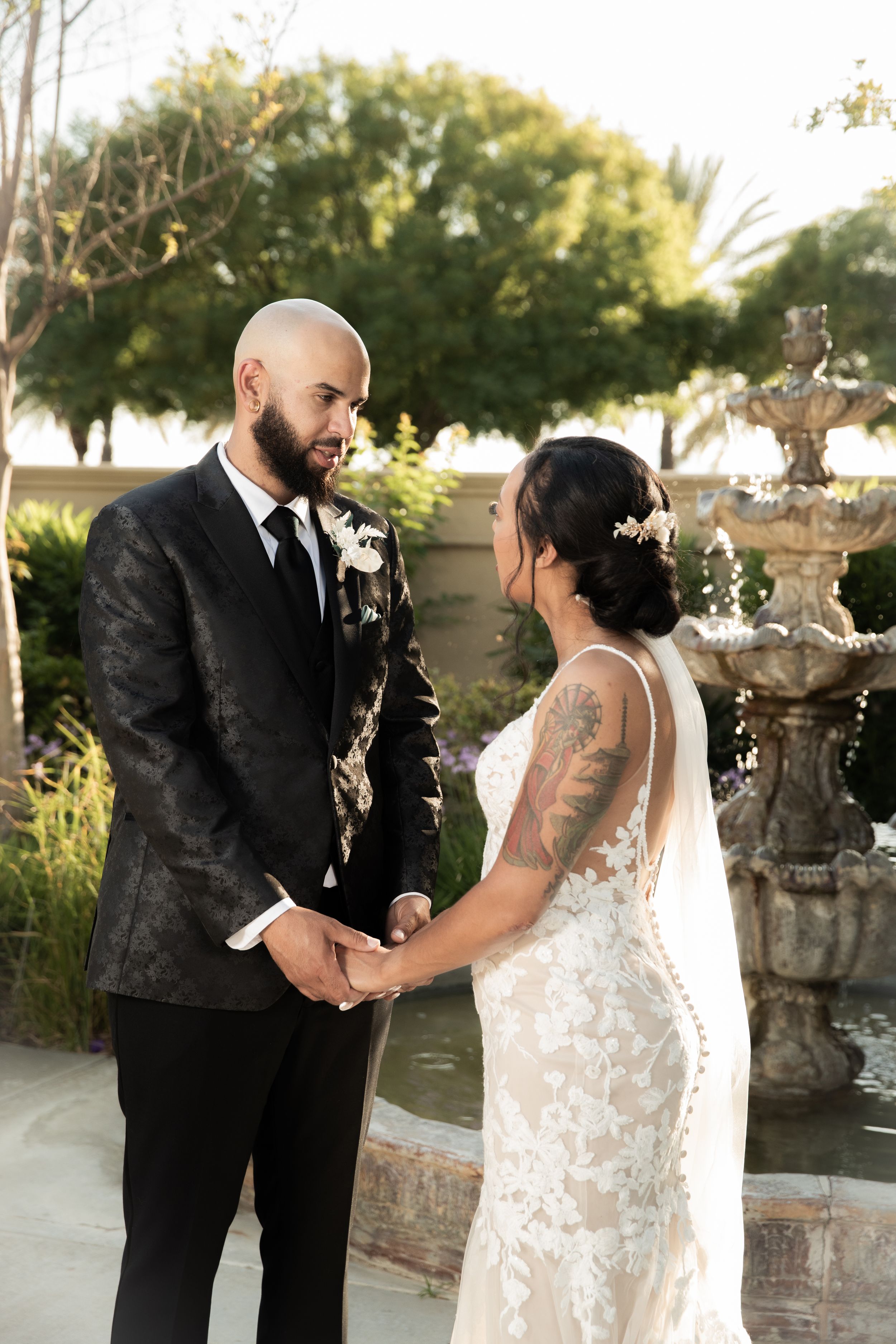 Wedding couple shares an intimate moment near a decorative garden fountain at sunset.