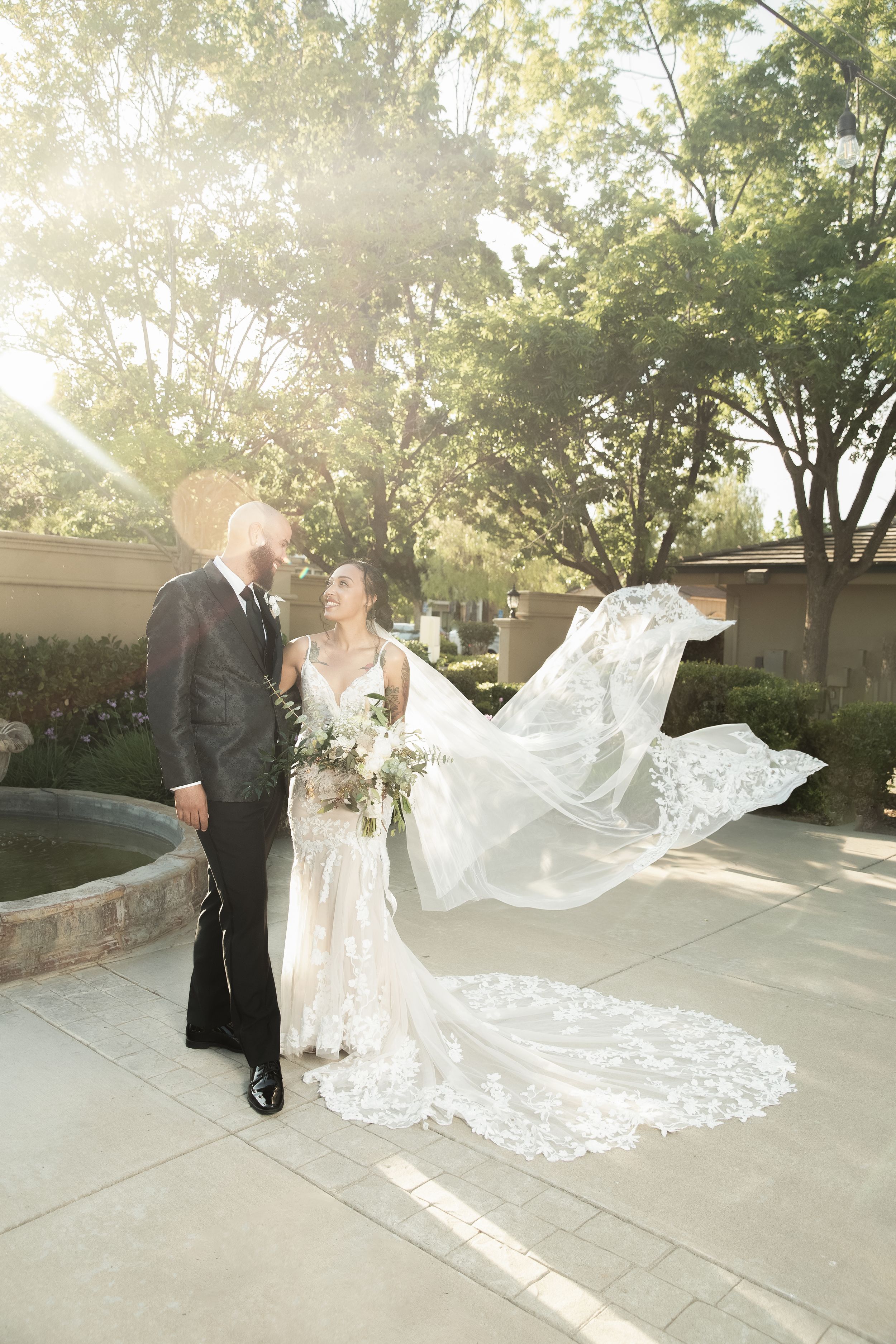 Romantic wedding photo with bride's veil flowing in the wind during golden hour.