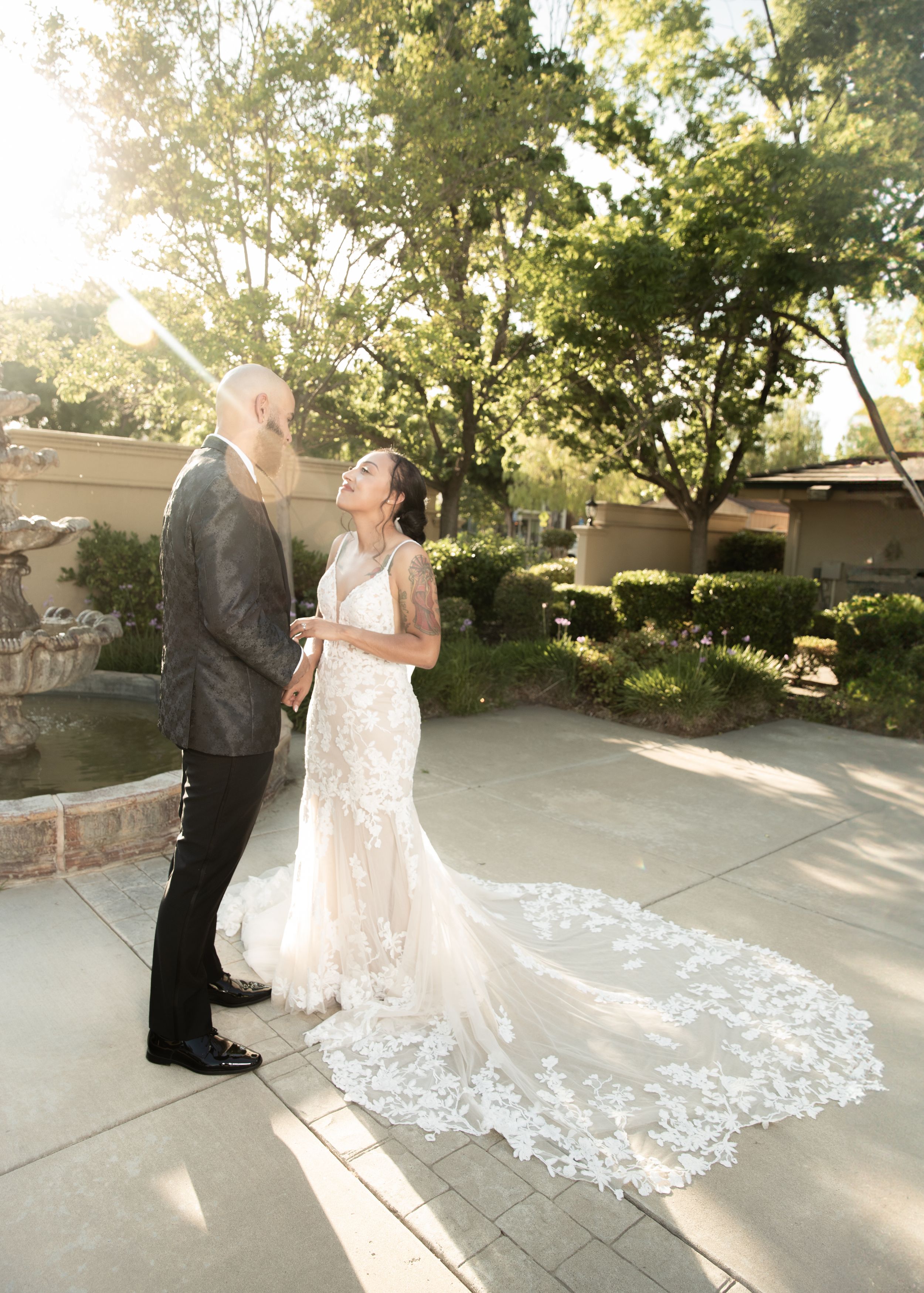 Newlyweds share a loving glance in a garden setting with lace wedding dress train.