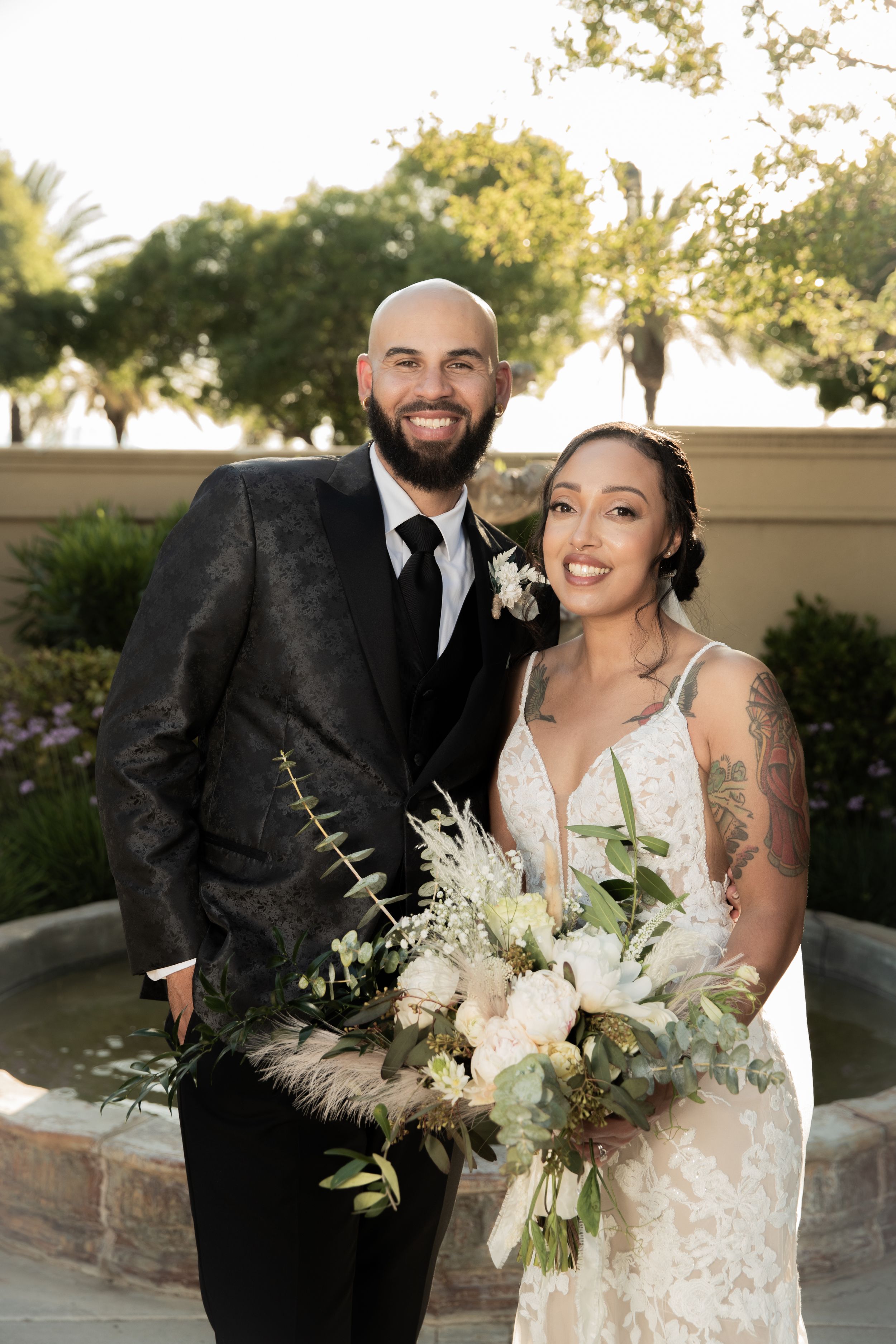 Elegant outdoor wedding portrait with bride holding white bouquet and groom in black suit.