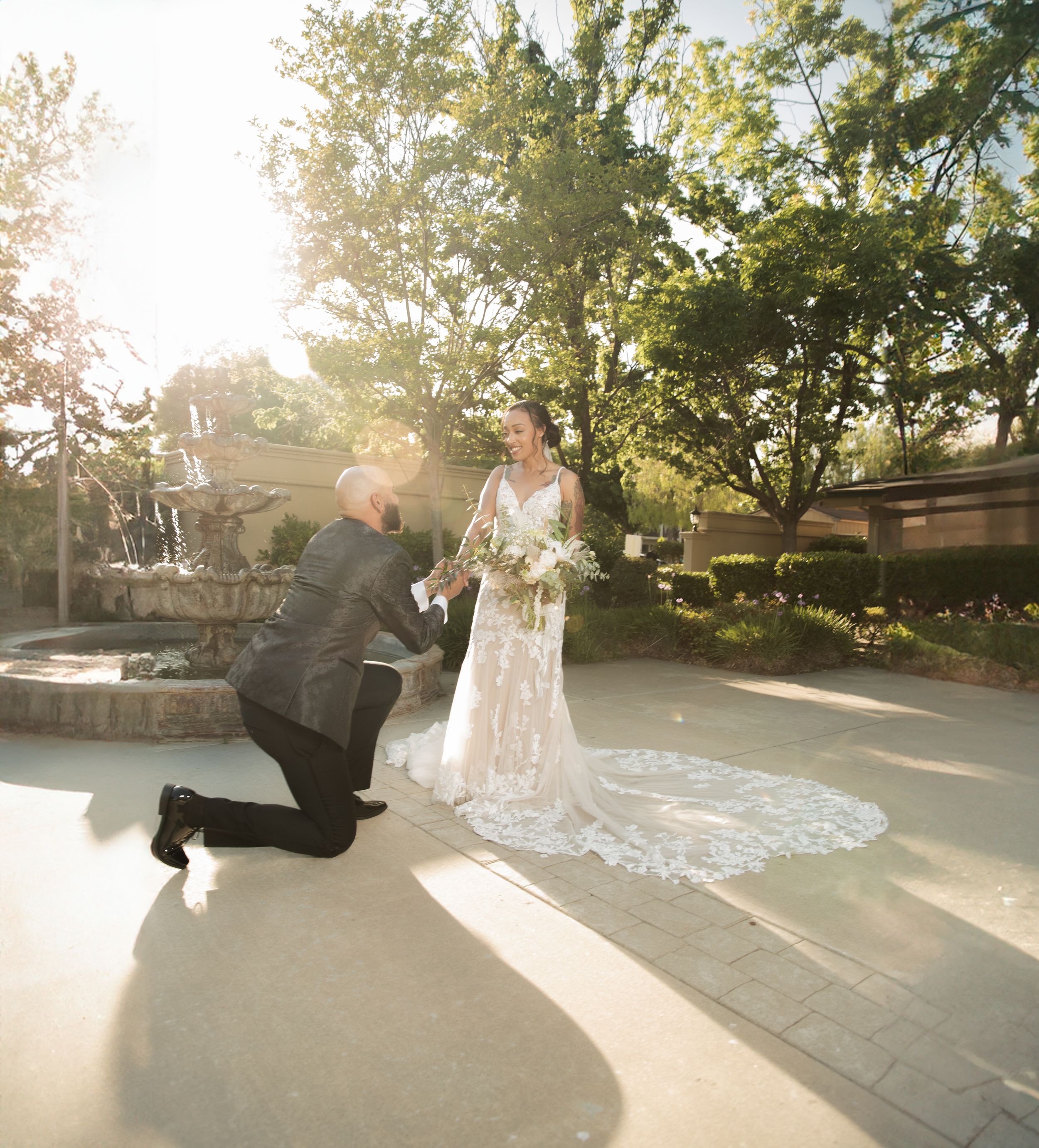 A romantic wedding proposal moment in front of an outdoor fountain during golden hour sunset.