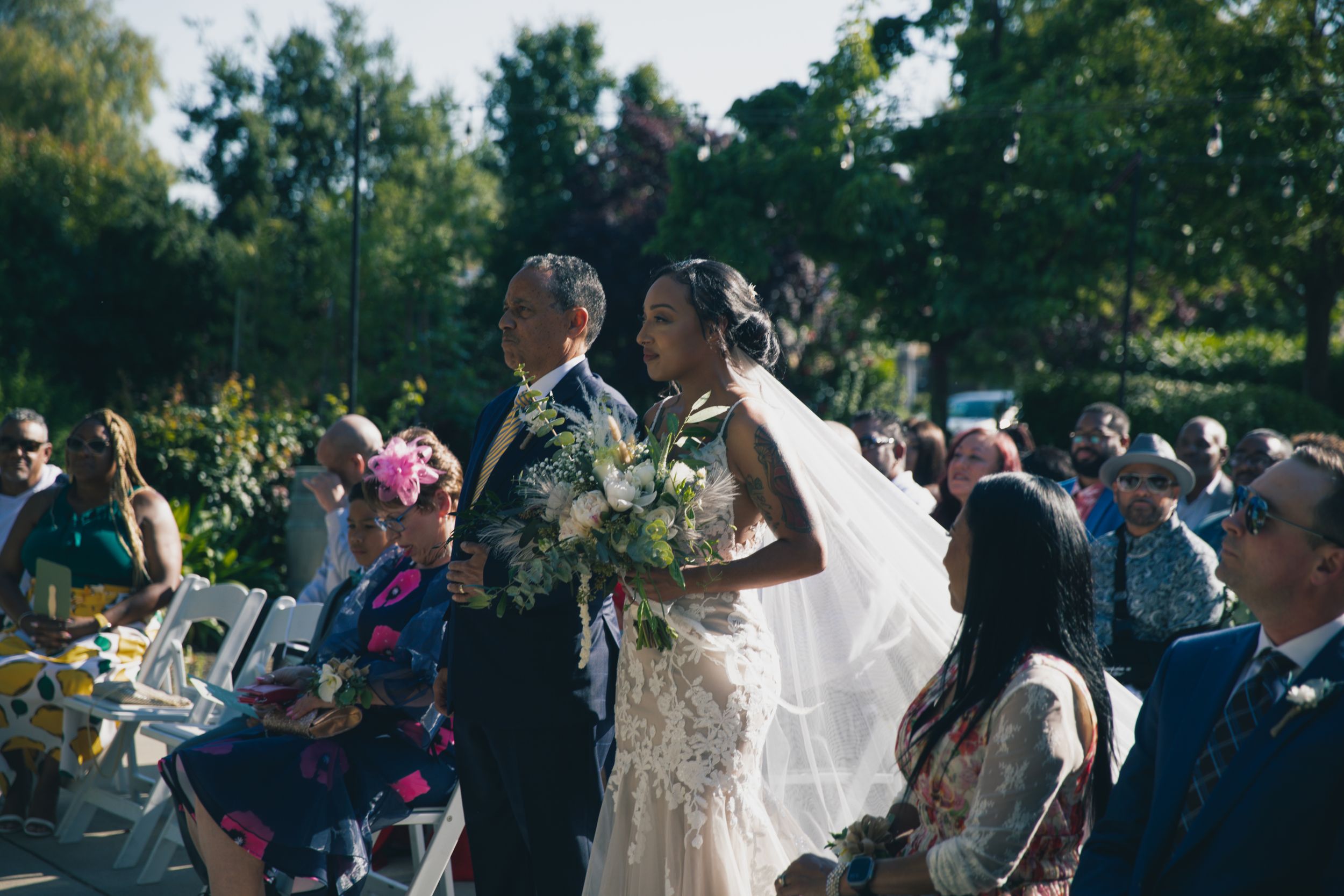 Outdoor wedding ceremony with guests watching couple exchange vows in garden setting.