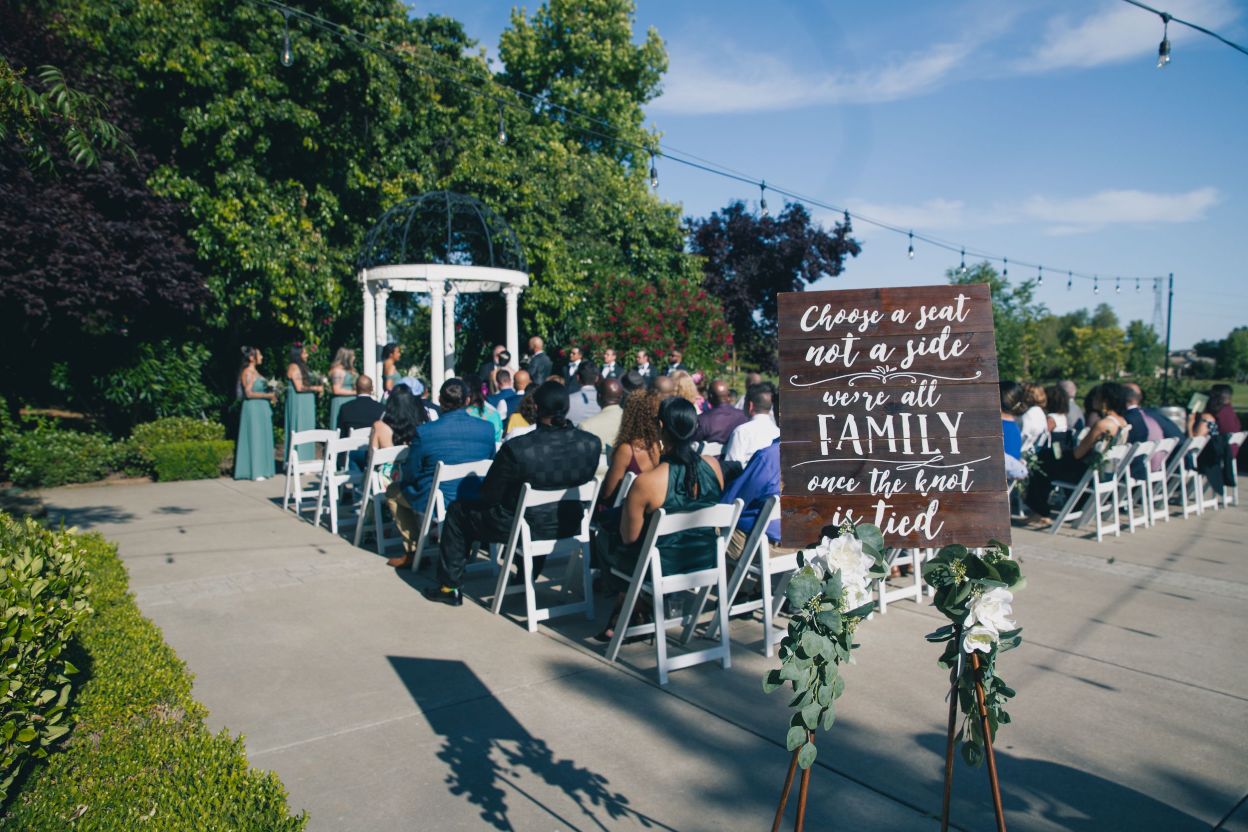 Garden wedding ceremony setup with white chairs and rustic welcome sign.
