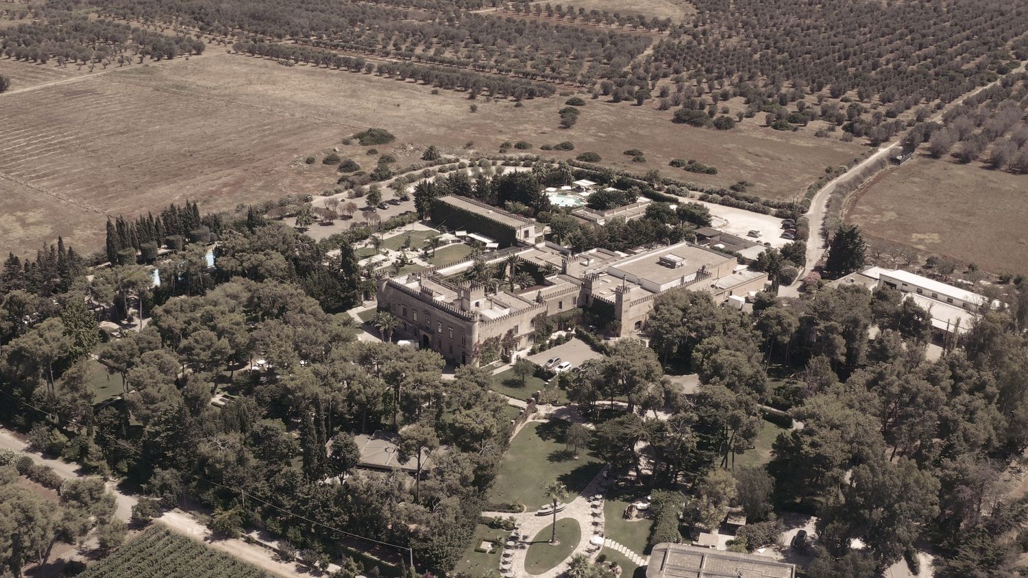 Aerial view of a sprawling estate with gardens and buildings in sepia tones.
