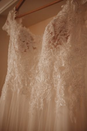 Close-up detail of delicate lace embellishments on a white wedding dress hanging on display.