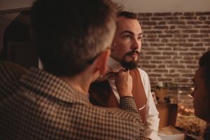 A person in a white vest being groomed with a vintage style aesthetic against a brick wall background.